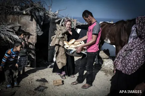 A Palestinian man carries fresh bread outside his tin shack in Khan Younis refugee camp, in southern Gaza Strip, November 21, 2013. The UNRWA, which is facing a 36-million dollar deficit, halted 19 out of 20 construction...