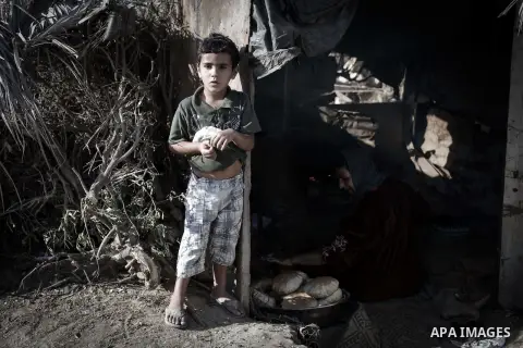 A Palestinian boy holds a loaf of bread as his mother bakes on firewood at her tin shack in Khan Younis refugee camp, in southern Gaza Strip, November 21, 2013. The UNRWA, which is facing a 36-million dollar deficit, hal...