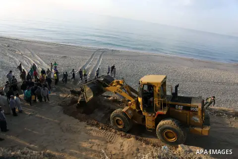 Palestinians watch as workers use a bulldozer to carry an old cannon which was found in the Mediterranean Sea off the coast of Deir al-Balah in central Gaza Strip, Tuesday, Nov. 26, 2013. Gaza Strip residents last month...