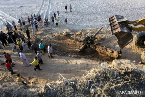 Palestinians watch as workers use a bulldozer to tow an old cannon which was found in the Mediterranean Sea off the coast of Deir al-Balah in central Gaza Strip, Tuesday, Nov. 26, 2013. Gaza Strip residents last month in...