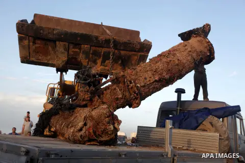 Palestinians watch as workers use a bulldozer to carry an old cannon which was found in the Mediterranean Sea off the coast of Deir al-Balah in central Gaza Strip, Tuesday, Nov. 26, 2013. Gaza Strip residents last month...