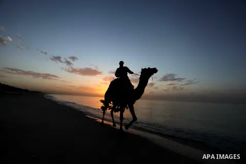 A Palestinian man rides a camel on the beach of the Mediterranean Sea during the sunset in Deir al-Balah in central Gaza Strip, Tuesday, Nov. 26, 2013. Photo by Ashraf Amra