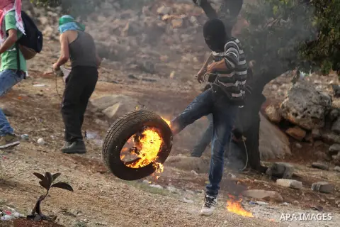 A Palestinian protester kicks a burning tyre during clashes between students from Bir Zeit University and Israeli security forces in the West Bank village of Betunia following a protest against the killing of three young...