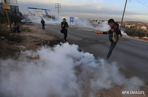 A Palestinian protester runs from tear gas fired by Israeli soldiers during a protest against Israel's plan of forced relocation for Bedouin residents in the southern Negev, outside the Beit El settlement near the West B...