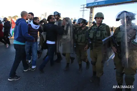 Palestinian protester are seen opposite Israeli settlers (background) during a demonstration against the Prawer plan at the gate of the Beit El settlement, near Ramallah, on November 30, 2013. The so-called Prawer-Begin...