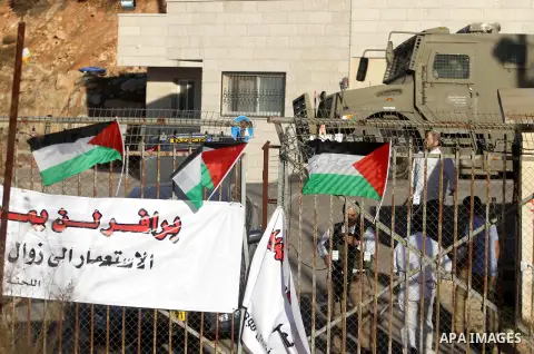 Palestinian protester are seen opposite Israeli settlers (background) during a demonstration against the Prawer plan at the gate of the Beit El settlement, near Ramallah, on November 30, 2013. The so-called Prawer-Begin...