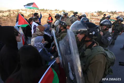 Palestinian protester are seen opposite Israeli settlers (background) during a demonstration against the Prawer plan at the gate of the Beit El settlement, near Ramallah, on November 30, 2013. The so-called Prawer-Begin...