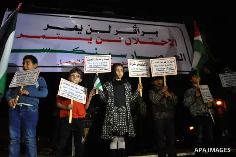 Palestinian children hold placards as others wave national flags during a protest against the siege of Gaza at the Unknown Soldier Square in Gaza City, Saturday, Nov. 30, 2013. Arabic writing in flames reads, "no to the...