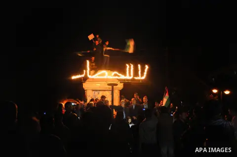 Palestinian children hold placards as others wave national flags during a protest against the siege of Gaza at the Unknown Soldier Square in Gaza City, Saturday, Nov. 30, 2013. Arabic writing in flames reads, "no to the...