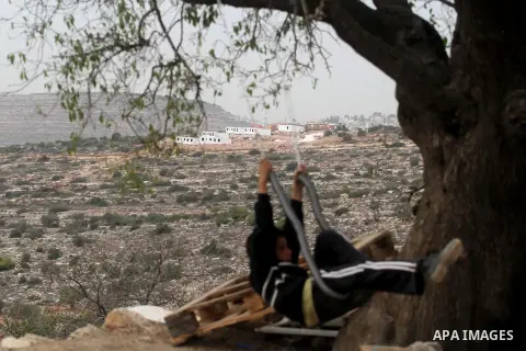 A Palestinian boy from the village of al-Mazraa al-Kubliyeh plays on a swing as bungalows built by Israeli settlers at an outpost constructed on seized land from the Palestinian village are seen in the background, near t...