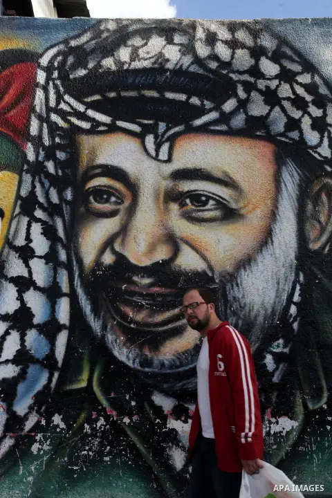 A Palestinian man walks pass a mural shows the late Palestinian leader Yasser Arafat, in Gaza City on Dec. 04, 2013 . Media reports on 03 December 2013 state that late Palestinian leader Yasser Arafat did not die of pois...