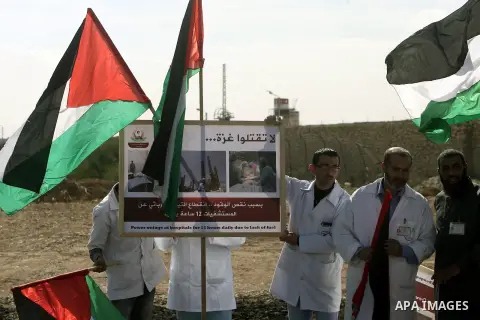 Palestinian doctors and patients hold a placard and flags at the gate of the Rafah border crossing point, on December 5, 2013, as Egyptian soldiers look on during a demonstration held by Palestinian doctors and patients...