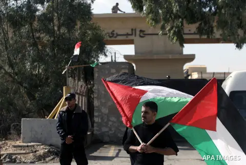 A Palestinian man holds flags at the gate of the Rafah border crossing point, on December 5, 2013, as Egyptian soldiers look on during a demonstration held by Palestinian doctors and patients demanding the permanent and...