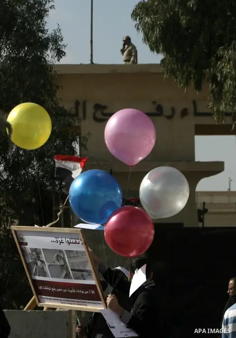 Palestinian doctors and patients hold placards and ballons at the gate of the Rafah border crossing point, on December 5, 2013, as Egyptian soldiers look on during a demonstration held by Palestinian doctors and patients...