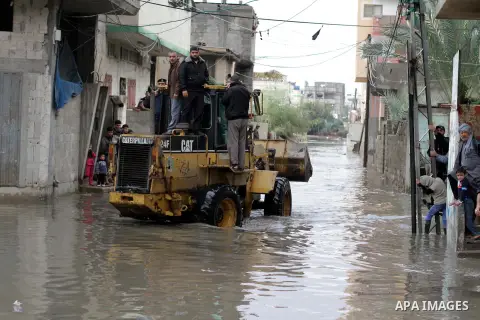 Palestinians ride a bulldozer in a flooded street following heavy rainfall in Gaza City on December 5, 2013. Photo by Ashraf Amra