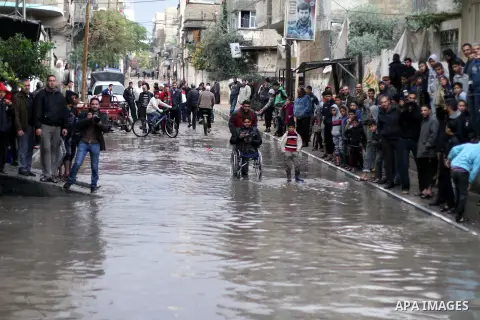 Palestinians watch as civil defence try to remove a car submerged in a flooded street following heavy rainfall in Gaza City on December 5, 2013. Photo by Ashraf Amra