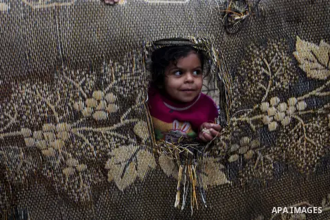 A Palestinian girl looks through a straw mat at a flooded street following heavy rainfall in Gaza City on December 5, 2013. Photo by Ashraf Amra