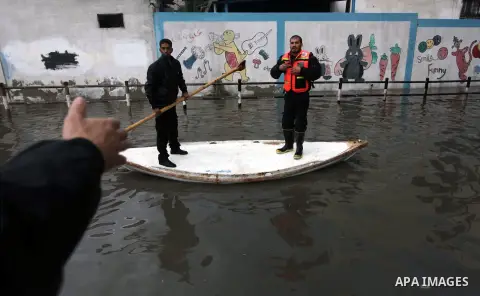 Palestinian civil defense arrive on a boat to help a Palestinian man after his car was submerged in a flooded street following heavy rainfall in Gaza City on December 5, 2013. Photo by Ashraf Amra