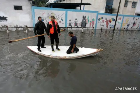 Palestinian civil defense arrive on a boat to help a Palestinian man after his car was submerged in a flooded street following heavy rainfall in Gaza City on December 5, 2013. Photo by Ashraf Amra