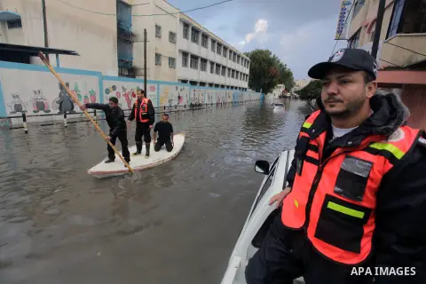 Palestinian civil defense arrive on a boat to help a Palestinian man after his car was submerged in a flooded street following heavy rainfall in Gaza City on December 5, 2013. Photo by Ashraf Amra