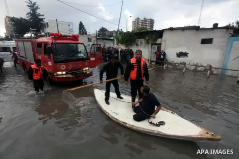 Palestinian civil defense arrive on a boat to help a Palestinian man after his car was submerged in a flooded street following heavy rainfall in Gaza City on December 5, 2013. Photo by Ashraf Amra