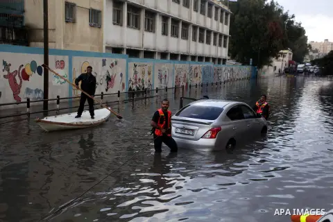 Palestinian civil defense arrive on a boat to help a Palestinian man after his car was submerged in a flooded street following heavy rainfall in Gaza City on December 5, 2013. Photo by Ashraf Amra