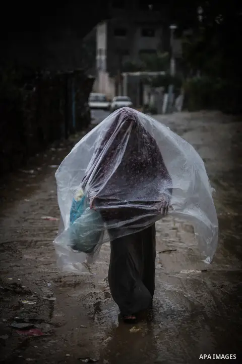 A Palestinian woman covers her body with a plastic sheet on her way to her house in heavy raining in Beit Lahiya, northern Gaza Strip, Thursday, Dec. 5, 2013. Heavy rains flooded most streets and blocked some of the stre...