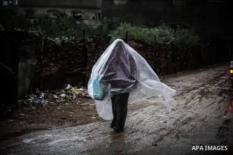 A Palestinian woman covers her body with a plastic sheet on her way to her house in heavy raining in Beit Lahiya, northern Gaza Strip, Thursday, Dec. 5, 2013. Heavy rains flooded most streets and blocked some of the stre...