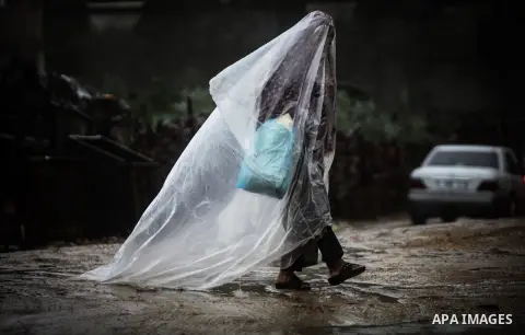 A Palestinian woman covers her body with a plastic sheet on her way to her house in heavy raining in Beit Lahiya, northern Gaza Strip, Thursday, Dec. 5, 2013. Heavy rains flooded most streets and blocked some of the stre...