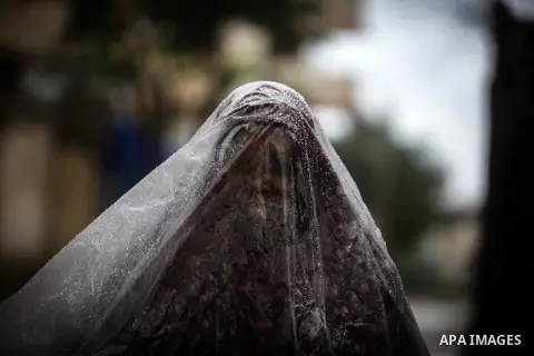 A Palestinian woman covers her body with a plastic sheet on her way to her house in heavy raining in Beit Lahiya, northern Gaza Strip, Thursday, Dec. 5, 2013. Heavy rains flooded most streets and blocked some of the stre...