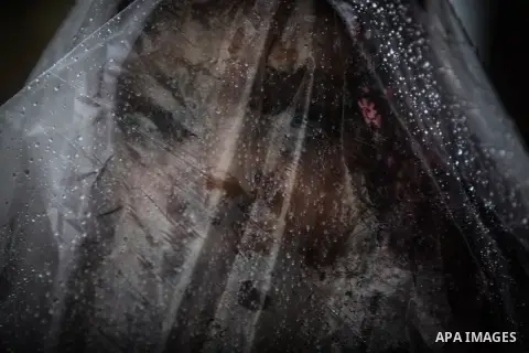 A Palestinian woman covers her body with a plastic sheet on her way to her house in heavy raining in Beit Lahiya, northern Gaza Strip, Thursday, Dec. 5, 2013. Heavy rains flooded most streets and blocked some of the stre...