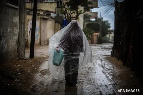 A Palestinian woman covers her body with a plastic sheet on her way to her house in heavy raining in Beit Lahiya, northern Gaza Strip, Thursday, Dec. 5, 2013. Heavy rains flooded most streets and blocked some of the stre...
