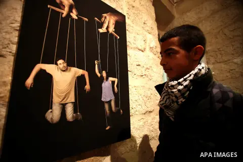 A Palestinian youth looks at a photo during a photogallery named 'Room Four', organised by French culture center in Jerusalem on Dec. 05, 2013. The photos by the artist Ashraf Dowani displayed in the photogallery and ref...