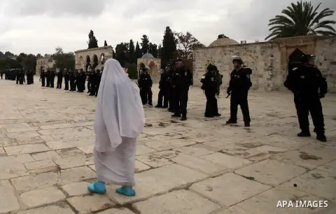 A Palestinian woman walks past Israeli riot police as they stand in the grounds of Jerusalem's al-Aqsa mosque compound during clashes with stone-throwers following Friday prayers, on December 6, 2013. Israeli police hurl...