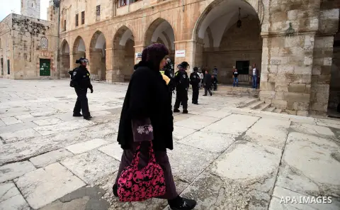 A Palestinian woman walks past Israeli riot police as they stand in the grounds of Jerusalem's al-Aqsa mosque compound during clashes with stone-throwers following Friday prayers, on December 6, 2013. Israeli police hurl...