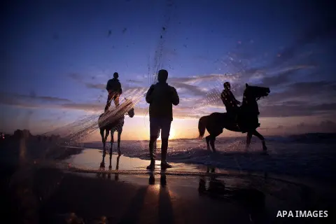 A Palestinian man fishing as others ride horses during the sunset on the beach of Gaza City, Dec. 06, 2013. British human rights organization Amnesty International condemned the Israeli blockade on the Gaza Strip in a st...