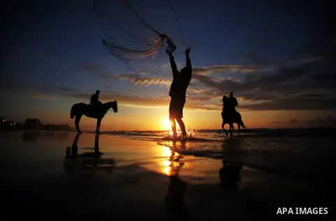 A Palestinian man fishing as others ride horses during the sunset on the beach of Gaza City, Dec. 06, 2013. British human rights organization Amnesty International condemned the Israeli blockade on the Gaza Strip in a st...