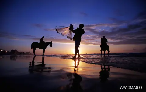 A Palestinian man fishing as others ride horses during the sunset on the beach of Gaza City, Dec. 06, 2013. British human rights organization Amnesty International condemned the Israeli blockade on the Gaza Strip in a st...