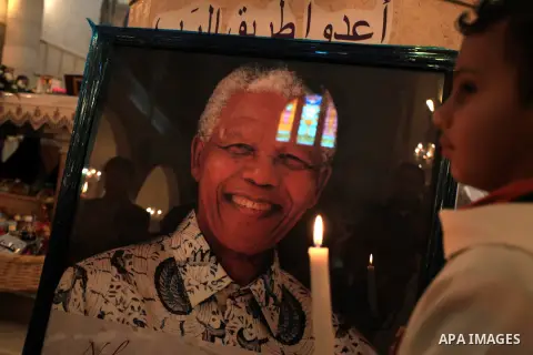 An alter boy stands with a candle infront of an image of the late South African leader President Nelson Mandela on display during a special Sunday service in his honour at the Holy Family Church in the West Bank city of...