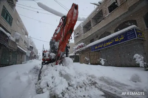 Palestinian workers use a bulldozer to remove snow in a street of the West Bank town of Hebron as snow falls on 14 December 2013. Reports state that the West Bank has been affected by a snowstorm, hitting Nablus, Ramalla...