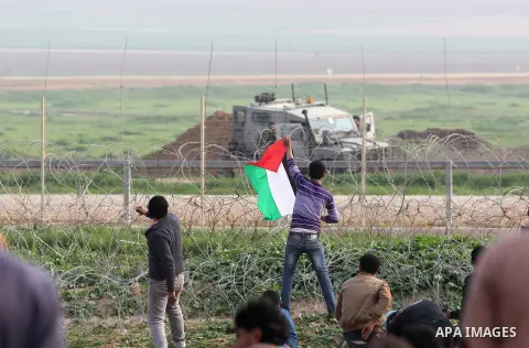 A Palestinian protester holds national flags during clashes with Israeli forces near the border with Israel, east of Jabalia refugee camp in northern Gaza Strip on February 14, 2014. The Israeli army fired live rounds an...