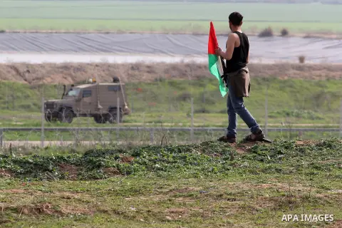 A Palestinian protester holds his national flag in front an Israeli military vehicle during clashes near the border with Israel, east of Jabalia refugee camp in northern Gaza Strip on February 21, 2014. The Israeli army...