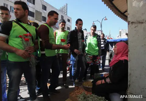 Palestinian youth distribute roses during a participate in the campaign " for the good, we gather" honoring for the elderly working women at the streets, in the West Bank city of Ramallah, on Feb. 22, 2014. Photo by Issa...