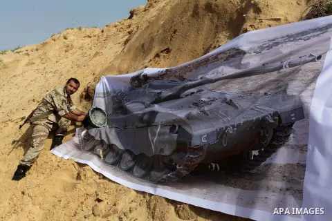 A photo taken on Feb. 23, 2014 shows a Palestinian actor dressed as a Hamas militant plants an improvised explosive device next to a photo of an Israeli tank during filming in a movie being made in Gaza called, ''Losing...