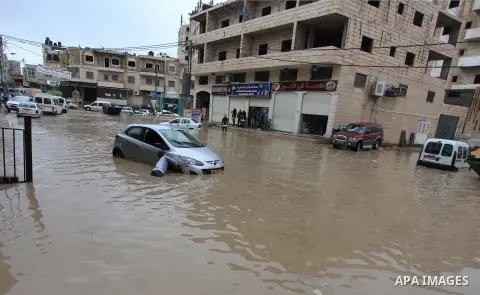 A Palestinian man tries to remove a car submerged in a flooded street during heavy rains on a stormy day, in the West Bank village of Kufr Aqab, northern Jerusalem on March 12, 2014. Photo by Issam Rimawi