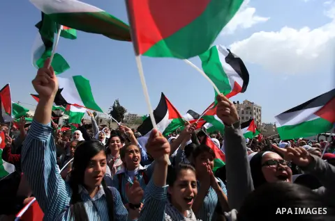 Palestinians wave their national flag as President Mahmud Abbas waves to his supporters following his trip to Washington DC, on March 20, 2014, in the West Bank city of Ramallah. US President Barack Obama and Palestinian...