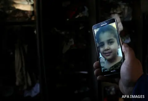 A Palestinian man holds a picture of Malak el-Eid, from phone, who was killed after a fire swept through her room in Rafah sothern in Gaza city on March 27, 2014. Gaza residents often use candles to light their house dur...