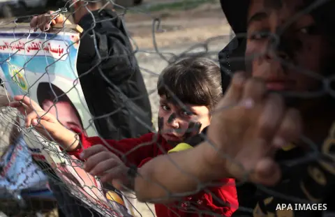 Palestinian children stand behind a fence as they watch a rally marking Palestinian Prisoner's Day organized by Islamic Jihad Movement, in the central Gaza Strip April 15, 2014. Photo by Ashraf Amra