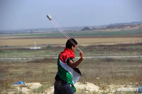 A Palestinian youth uses a slingshot to hurl stones at Israeli security forces during clashes near the border with Israel, east of Jabalia refugee camp in northern Gaza Strip, May 21, 2014 .Rallies in support of the hung...