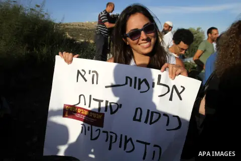 An Israeli army reservist holds a placard during a demonstration against settlers' phenomenon of so-called "price tag" attacks, outside the Yitzhar Jewish settlement, near the West Bank city of Nablus, May 18, 2014. The...